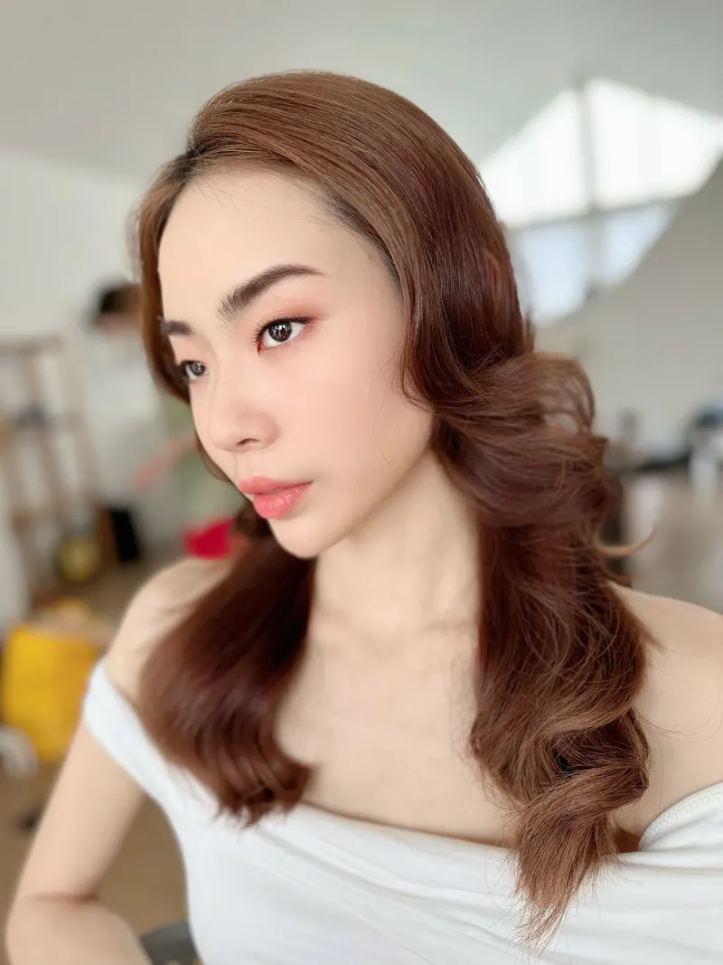 ผมสีน้ำตาลแดงลอนใหญ่ปัดด้านข้าง สวมเสื้อสีขาวเปิดไหล่ แต่งตาธรรมชาติ ลิปสีชมพูกุหลาบ มองไปด้านข้างในห้องสว่าง