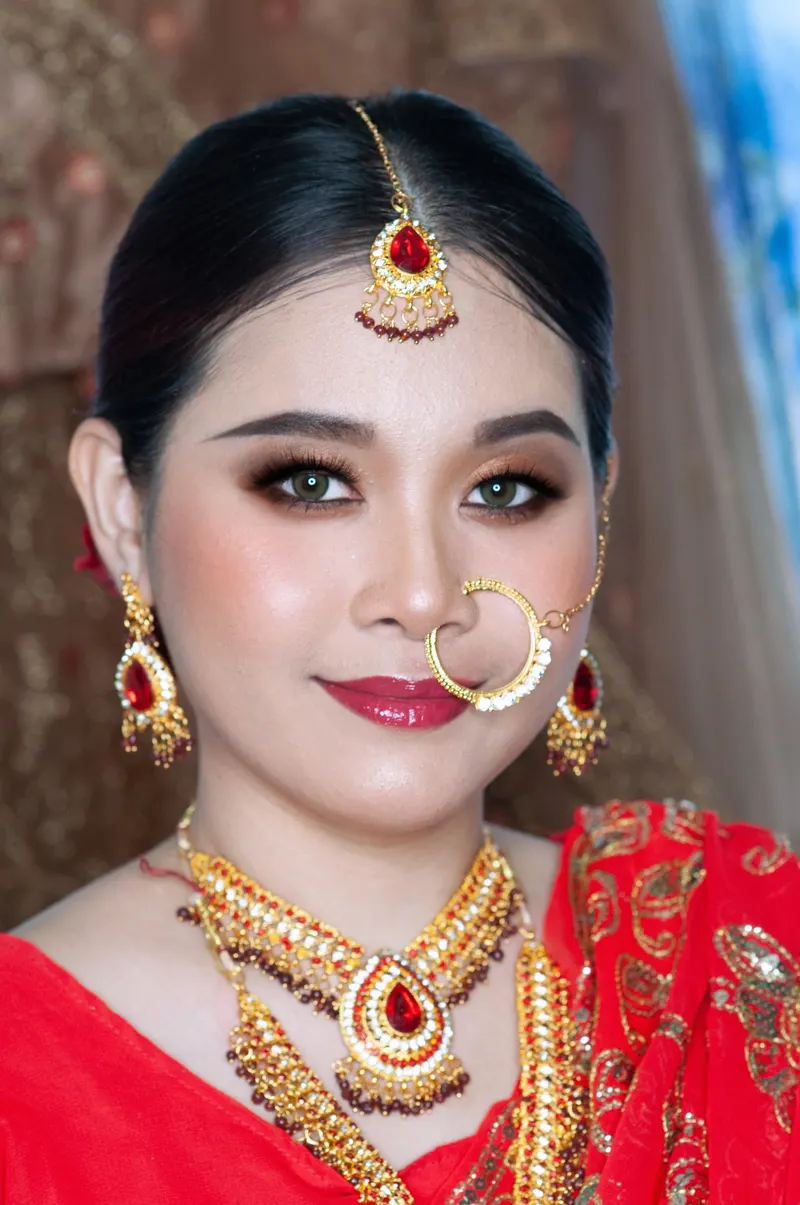 ลุคอินเดียสวมเครื่องประดับหน้าผากและห่วงจมูกทอง ต่างหูทับทิมสีแดง ชุดสีแดงสด แต่งตาสโมกกี้สีน้ำตาลดำ ลิปสีแดงเบอร์รี