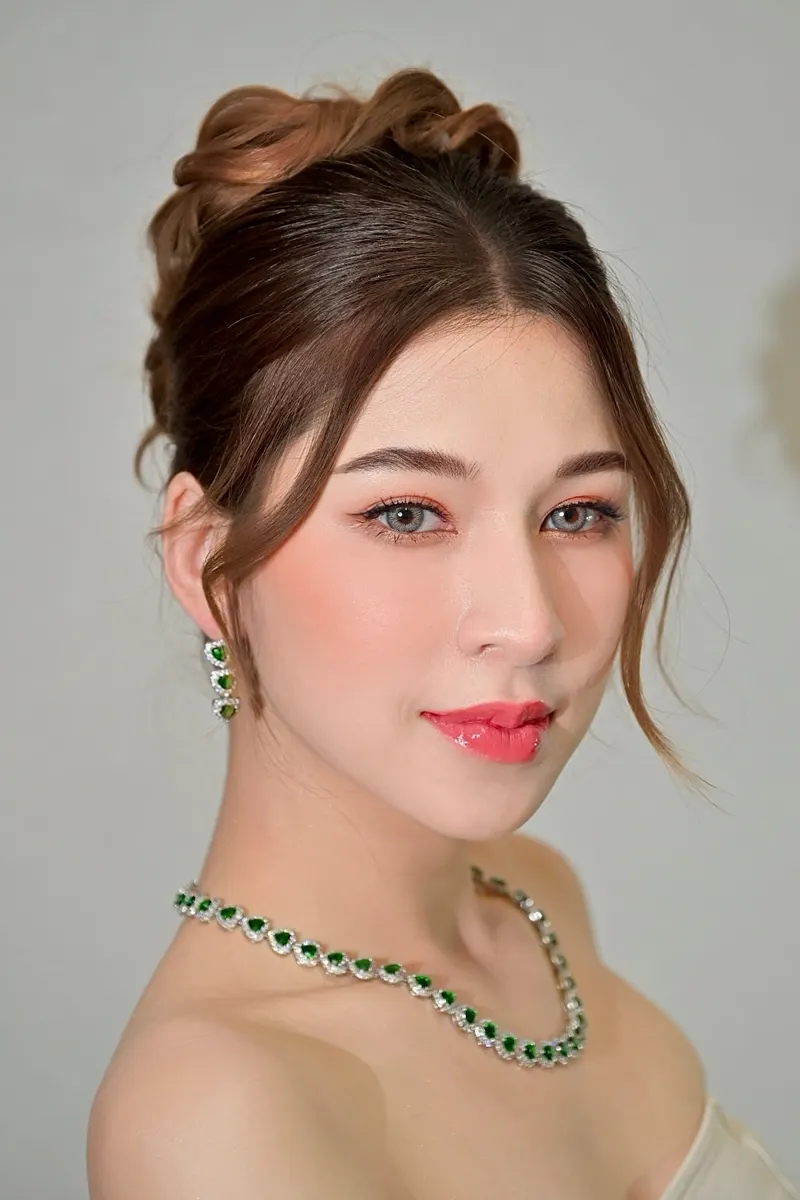 ผมน้ำตาลทองเกล้ามวยสูง ปล่อยปอยข้างหน้า สร้อยคอและต่างหูมรกตหัวใจ แต่งตาส้มพีช ปัดแก้มพีชชมพู ลิปกลอสสีชมพูเข้ม