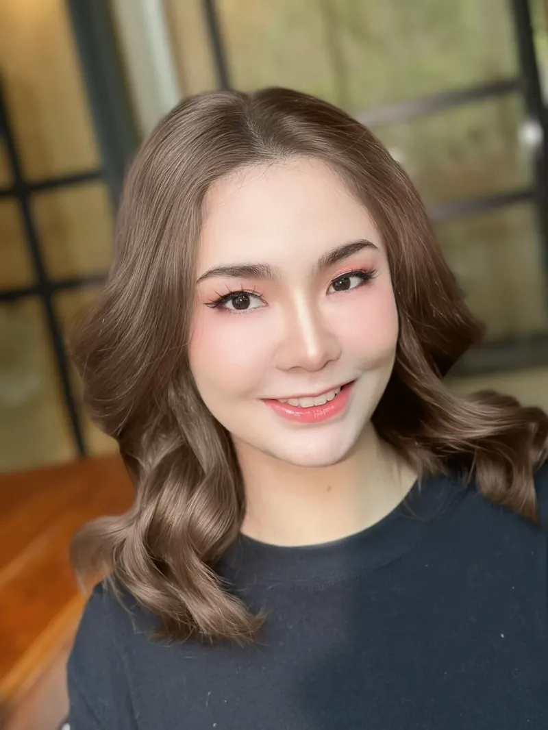 ผมน้ำตาลเข้มลอนปลายผม ใส่เสื้อยืดสีดำ ยิ้มเห็นฟัน แต่งตาโทนชมพูพีช ลิปสีส้มพีช ฉากหน้าต่างเหล็กดำ