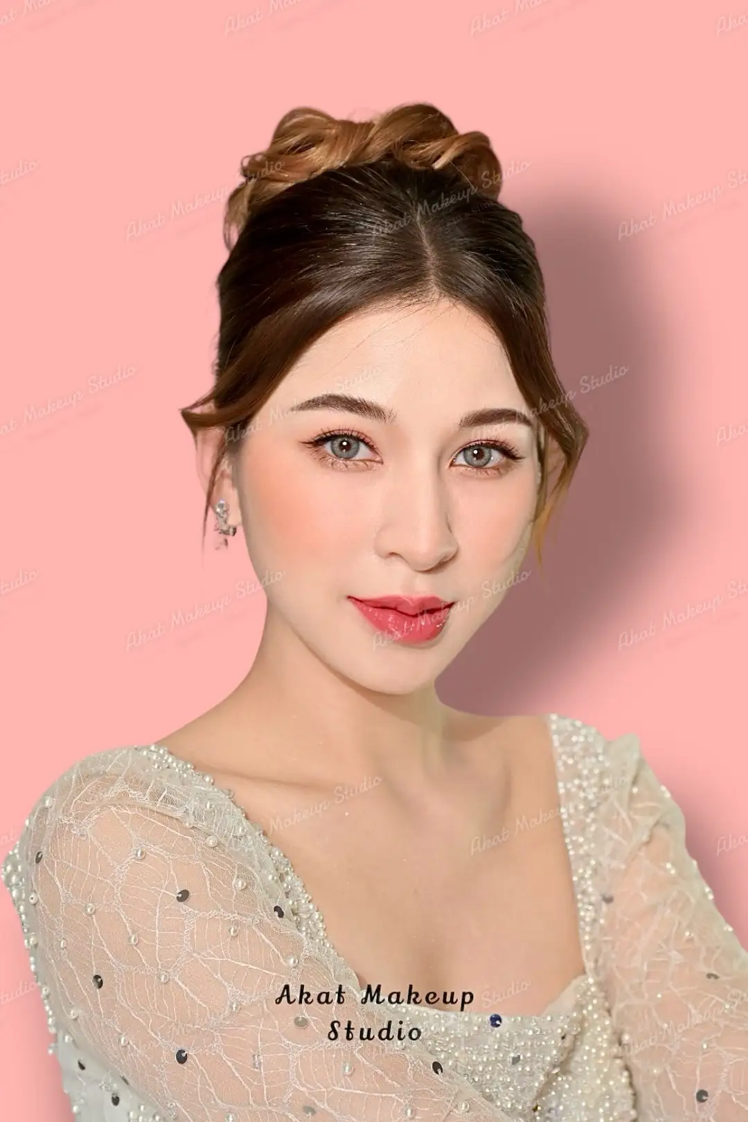 เจ้าสาวชุดวิวาห์ลูกไม้ปักไข่มุก ผมเกล้ามวยสูง แต่งตาโทนธรรมชาติ ปากสีแดง ยิ้มบาง ๆ บนฉากสีชมพูพาสเทล