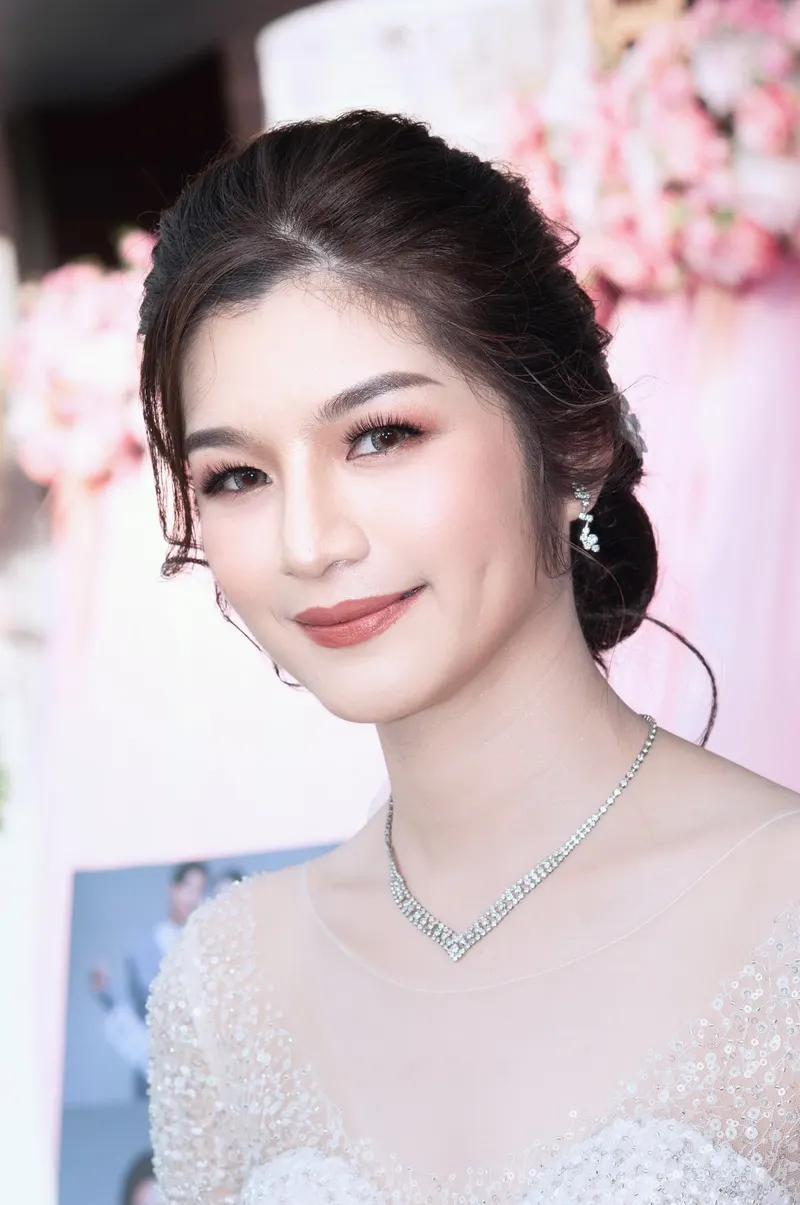 เจ้าสาวชุดเจ้าหญิงลูกไม้ประดับคริสตัล สร้อยคอเพชรรูปตัววี ผมรวบต่ำเก็บเรียบ แต่งตาโทนน้ำตาลชมพู ลิปสีกุหลาบ ฉากดอกไม้ชมพู
