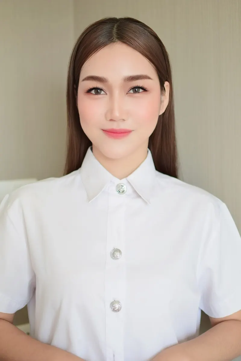 ผมตรงสีน้ำตาลเข้มสยายยาว แต่งหน้าบางเบาโทนธรรมชาติ ลิปสีชมพูนู้ด เสื้อนักศึกษาสีขาวกระดุมเงิน ยืนมือประสานด้านหน้า