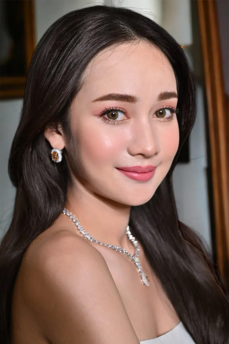 ภาพถ่ายใกล้แต่งหน้าถ่ายแบบ ผมดำยาวสลวย สวมต่างหูและสร้อยเพชรเปิดไหล่ ตาโทนชมพูพีช ลิปชมพูกุหลาบ ปัดแก้มบาง ฉากกรอบกระจกทอง