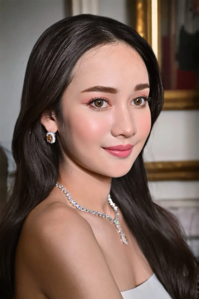 ภาพถ่ายแบบผมดำยาวเปิดไหล่ สร้อยคอเพชรและต่างหูอัญมณีสีส้ม แต่งตาโทนพีชชมพูเรียบหรู ลิปสีชมพูกุหลาบ ผิวเนียนสว่างใส