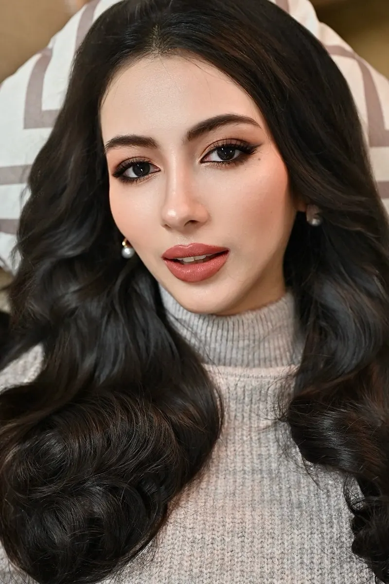 ภาพใกล้นางแบบผมดำลอนใหญ่ สวมไหมพรมคอเต่าสีเบจ ขอบตาเขียนลายเส้นเฉียง ปัดแก้มโทนอิฐ ลิปสีน้ำตาลส้ม ต่างหูไข่มุก
