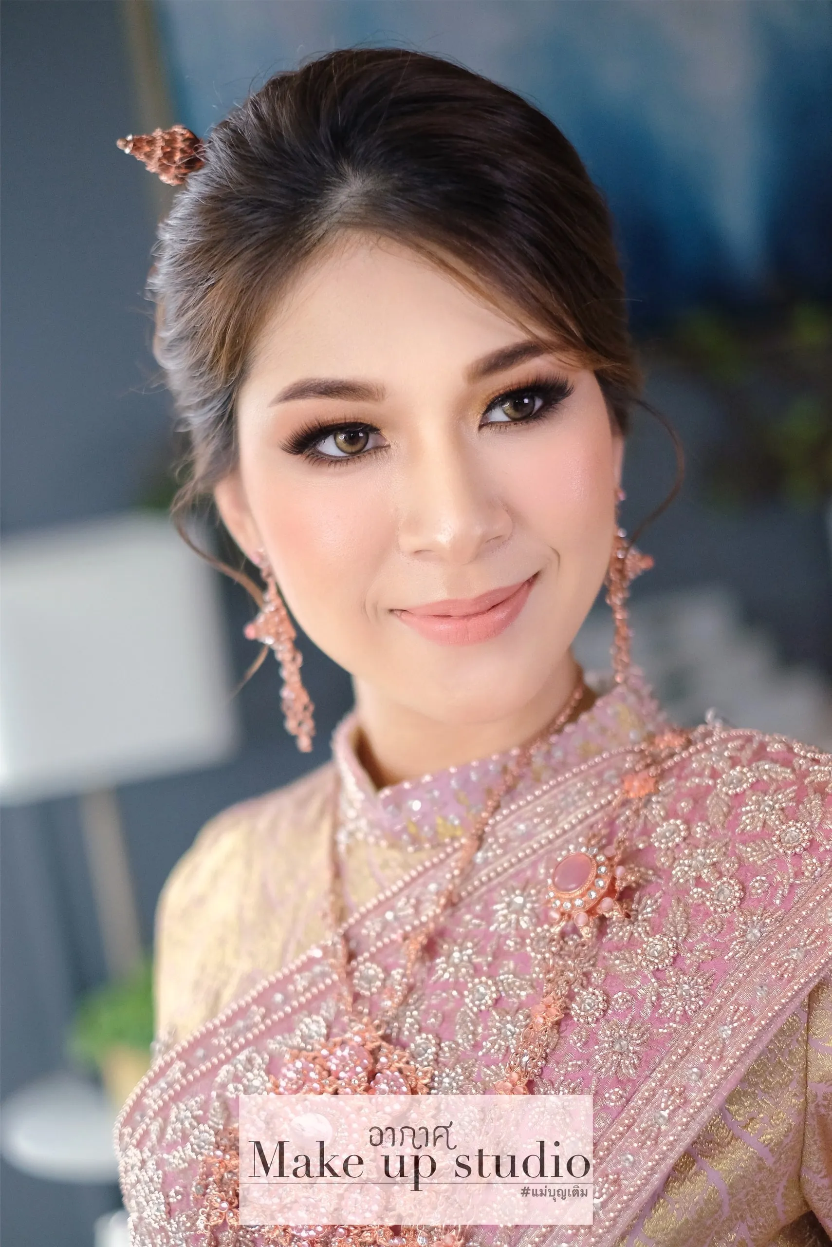 เจ้าสาวชุดไทยสีชมพูโอรสประดับลูกปัดและเลื่อม ติดปิ่นปักผมสีโรสโกลด์ ต่างหูห้อยยาว แต่งตาสโมกกี้น้ำตาลนุ่ม ลิปนู้ดชมพู ยิ้มบาง ๆ